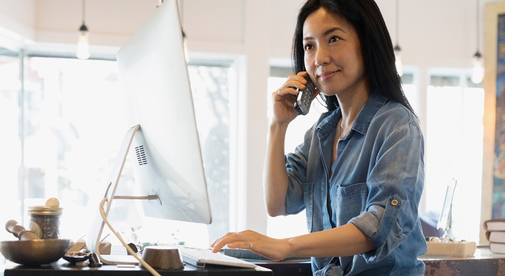Woman on mobile phone sitting at a monitor
